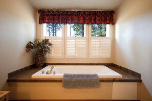 Ein Badezimmer mit einer Badewanne, einem Fenster mit Fensterläden und einer Vase mit Blumen.