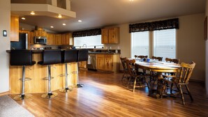 Una cocina con armarios de madera, una barra con taburetes, una mesa de comedor con sillas y un horno empotrado.