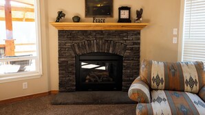 Un salón con chimenea de piedra, un repisa de madera con un reloj y un cuadro enmarcado, y un sofá estampado.