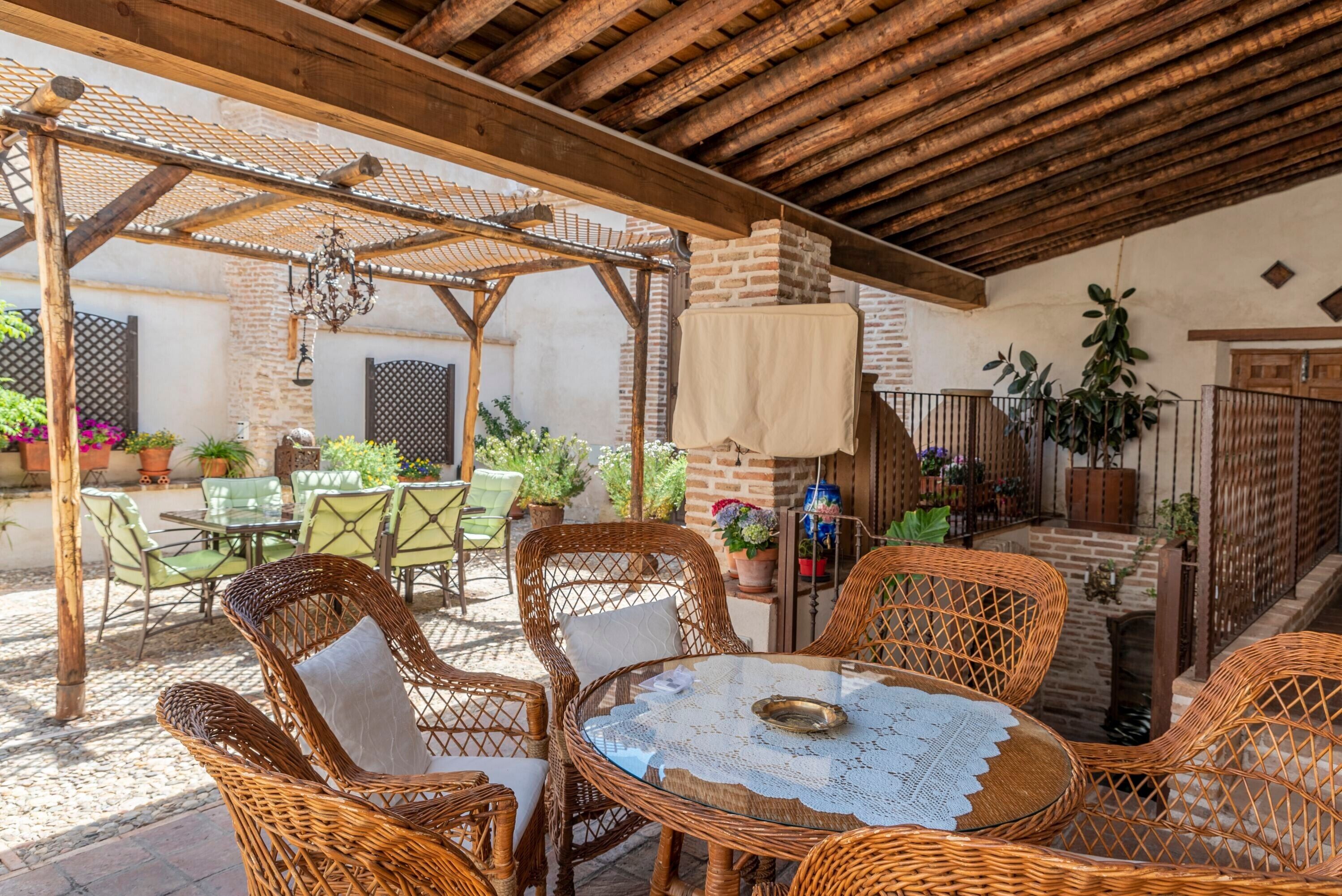 A covered outdoor patio with wicker furniture, a table with a lace tablecloth, and potted plants.