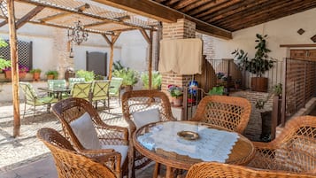 A covered outdoor patio with wicker furniture, a table with a lace tablecloth, and potted plants.