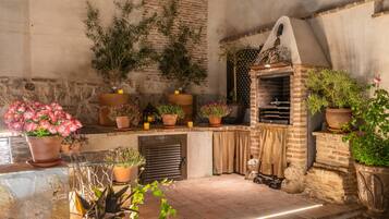 Un espacio exterior rústico con un horno de ladrillo, plantas en macetas y un muro de piedra.