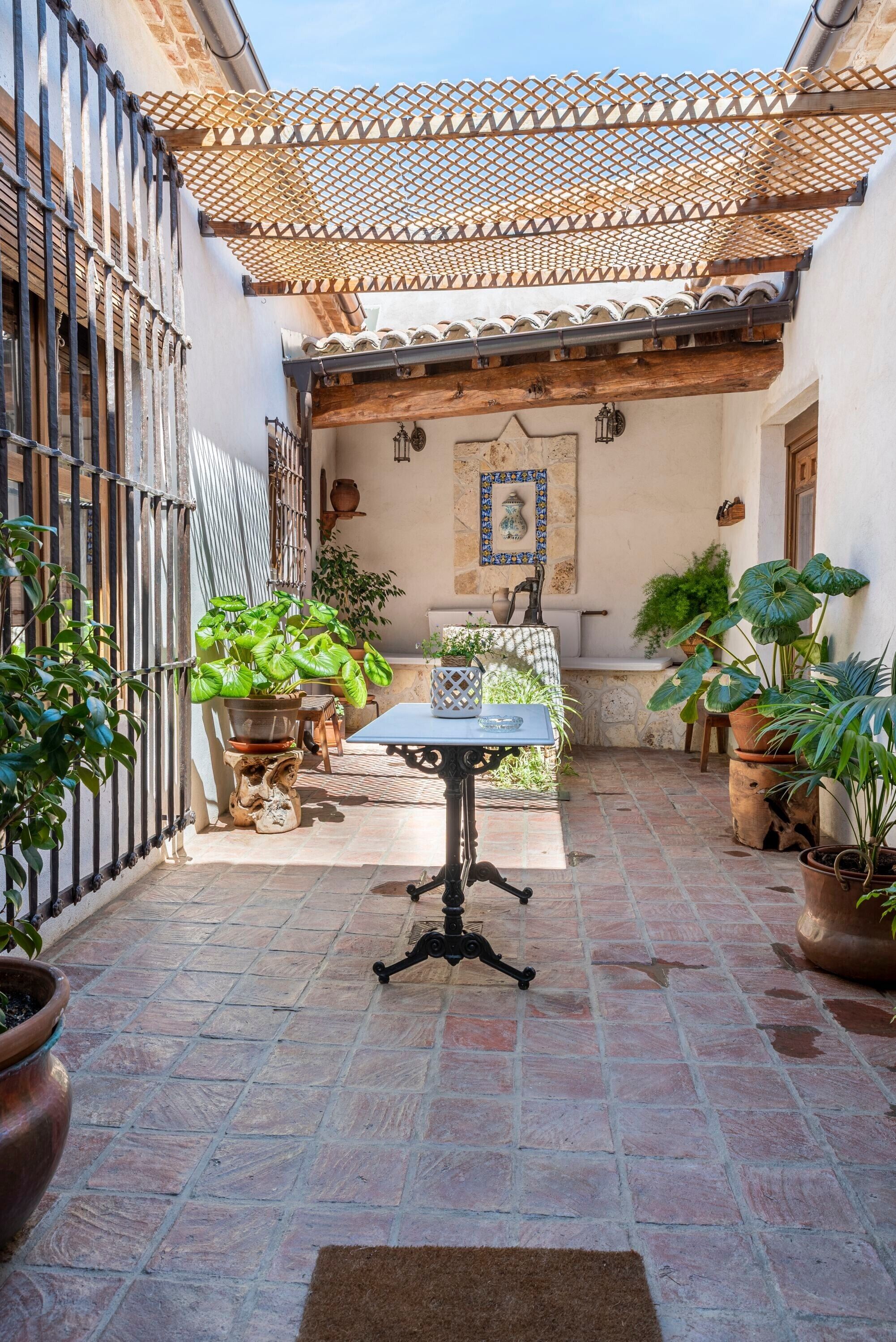 A courtyard with a table and chairs, potted plants, a tiled floor, and a wooden pergola.