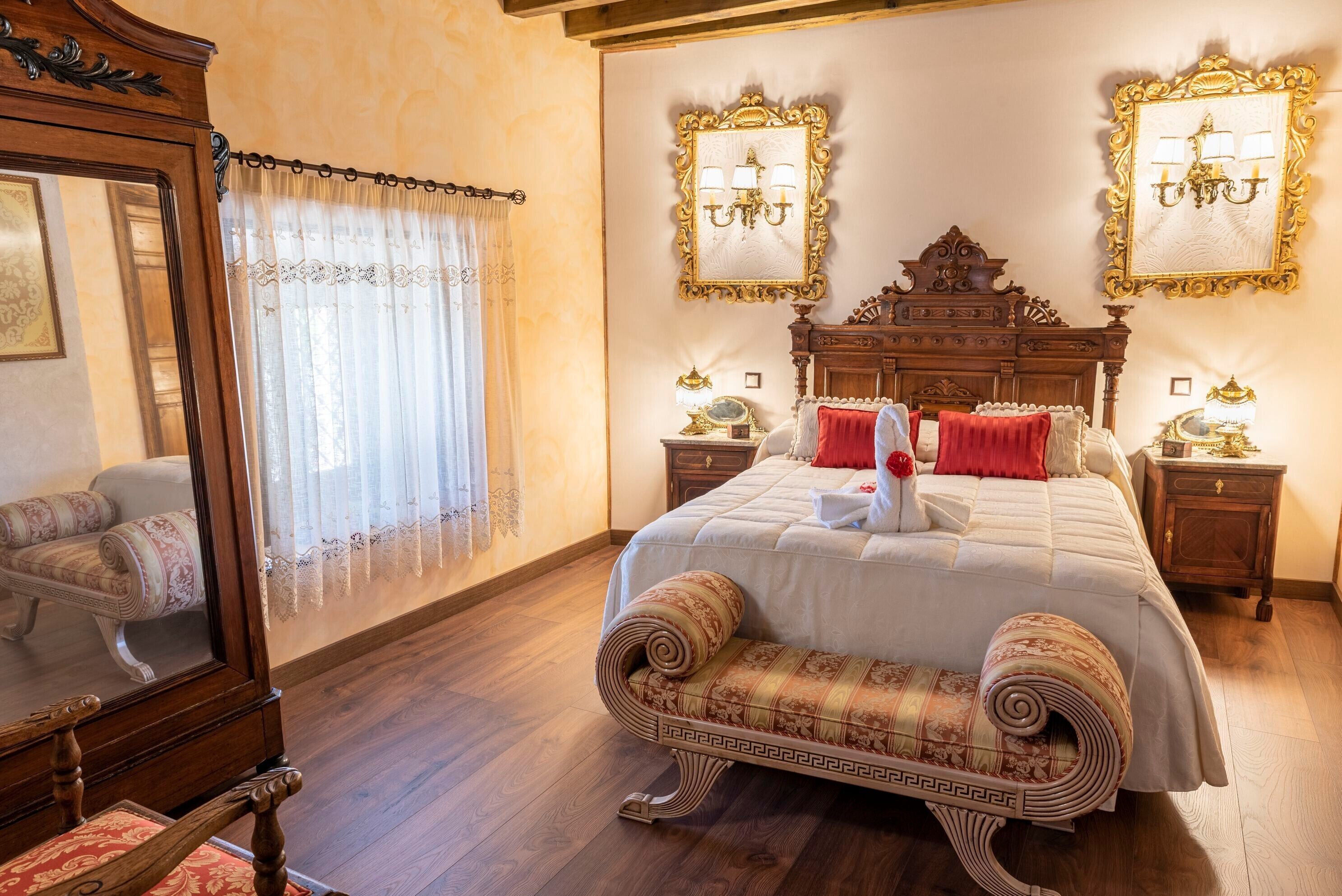 A bedroom with a large bed, two nightstands, a wooden bench, and a mirror.