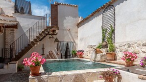 Une cour avec une piscine, des murs en pierre, un escalier et des plantes en pot.