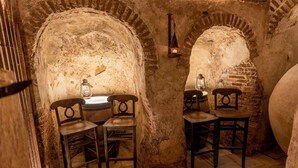 Une pièce rustique aux murs de pierre, avec deux chaises en bois, une petite table et une lanterne.