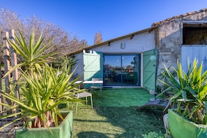 A patio with a table and chairs, a small garden with plants, and a building with a glass door.