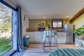 A compact kitchen with a dining area, a refrigerator, and a window overlooking a garden.