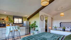 Una cocina compacta con zona de comedor, una cama con manta verde y un reloj en la pared.