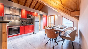 Una cocina moderna con armarios rojos, electrodomésticos de acero inoxidable y un comedor con una mesa dispuesta para cuatro.