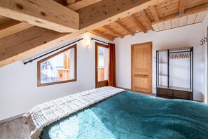 Ein Zimmer mit Bett, Holzbalken, einem Fenster und einer Tür.