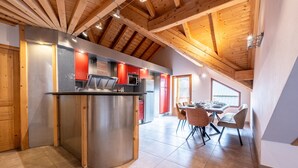 Una cocina moderna con una isla central, vigas de techo de madera y un comedor con sillas y una mesa.