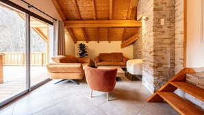 Una sala de estar moderna con techo de madera, pared de piedra y ventanas amplias.