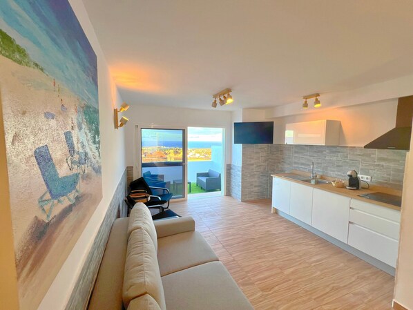 Uma sala de estar moderna com um sofá, um quadro e vista para o mar.