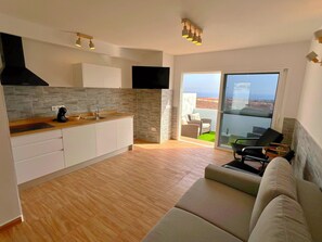 Cozinha moderna com forno embutido, área de refeições com sofá e varanda com vista.