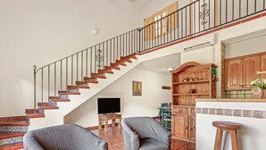 A living room with a staircase, two armchairs, a wooden coffee table, and a kitchen area with wooden cabinets and a bar counter. - Villa '25 Lola Flores' with Private Terrace, Wi-Fi and Air Conditioning (Ramatuelle)