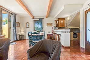 Amplia sala de estar con una mesa de comedor, sillas y un sofá. Se observa una cocina con armarios de madera y una lavadora al fondo.
