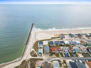 Vue aérienne d’une zone résidentielle côtière, avec des maisons, une plage et une jetée.