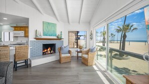 Ein geräumiges Wohnzimmer mit Kamin, Rattanmöbeln und einem großen Fenster mit Blick auf einen Strand.