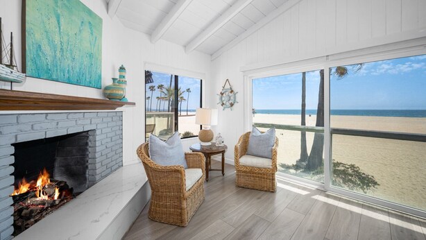 Ein Zimmer direkt am Strand mit Kamin, Korbsesseln, einem Tisch mit Lampe und Blick auf den Strand.