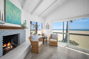 Une chambre située en bord de mer, dotée d'une cheminée, de fauteuils en osier, d'une table avec une lampe et offrant une vue sur la plage.