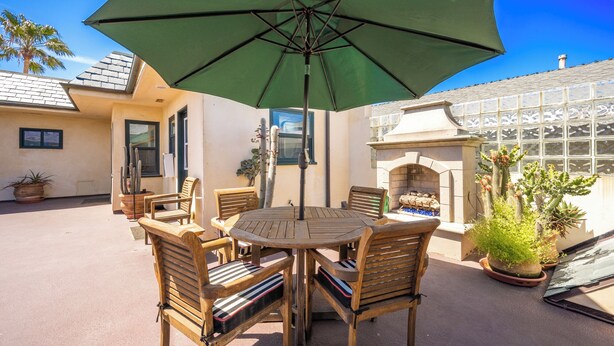 A patio with a round wooden table and four chairs, an umbrella, and a cactus plant. - Apt next to Boardwalk, Pier, Beach, Dining & More (Newport Beach)