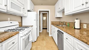 A kitchen with white cabinets, a gas stove, a refrigerator, a dishwasher, granite countertops, and a tiled floor. - Clean Budget Friendly Apartment Steps from Beach (Newport Beach)