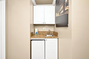 Compact kitchen with white cabinetry, granite countertop, and a dishwasher, sink, and framed picture.