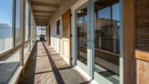A corridor with wooden flooring, large windows, and a door leading to a kitchen area.