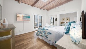 A bedroom with a wooden ceiling, a bed with a floral bedspread, a large window, and a desk with a ship model.