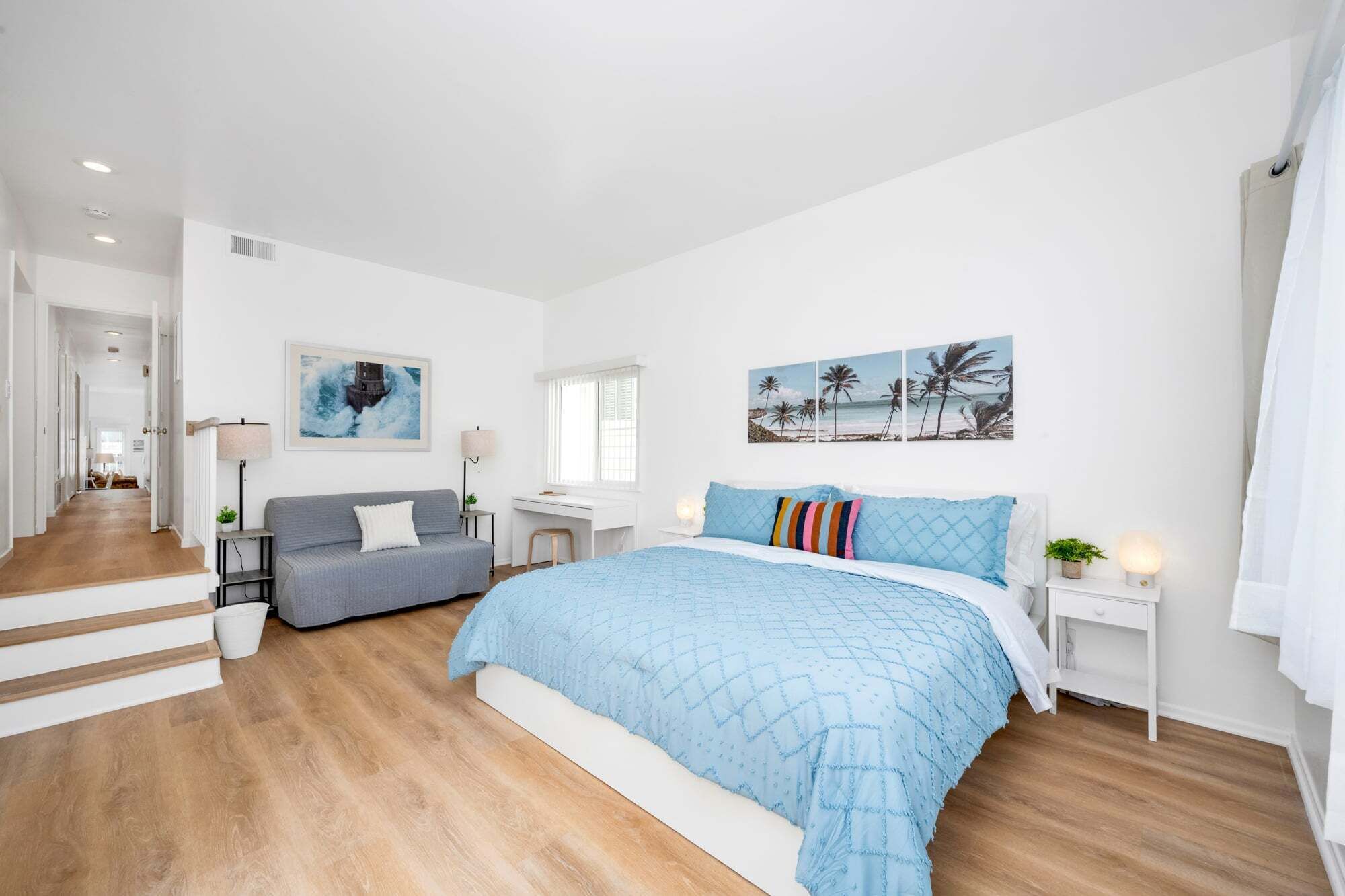 A bedroom with a bed, a desk, a sofa, and a staircase.