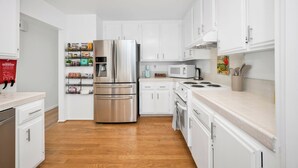 Una cucina moderna con mobili bianchi, elettrodomestici in acciaio inossidabile e pavimento in legno.