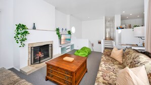 Un soggiorno moderno con camino, tavolino in legno, divano decorato e un pouf verde.