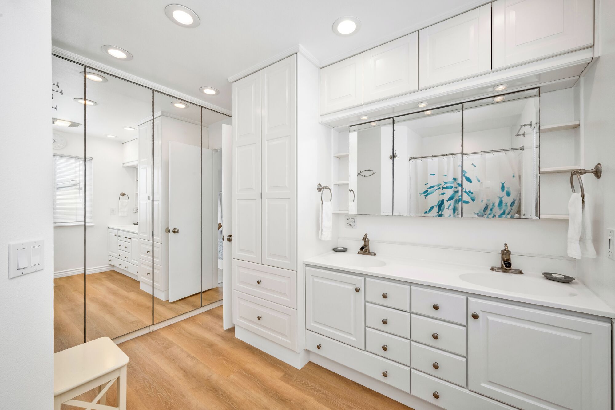 A modern bathroom with white cabinetry, a large mirror, and a wooden floor.