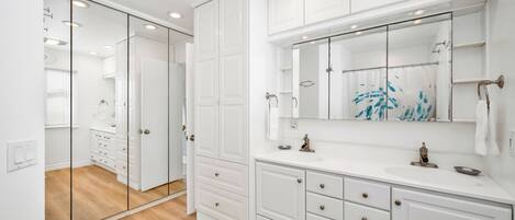 A modern bathroom with white cabinetry, a large mirror, and a wooden floor.