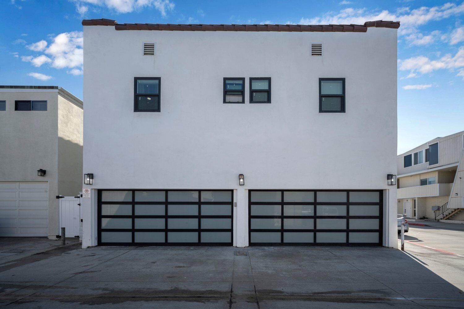 Un bâtiment à deux étages, doté d’une façade blanche, de deux portes de garage et d’une petite rangée de fenêtres à l’étage supérieur.