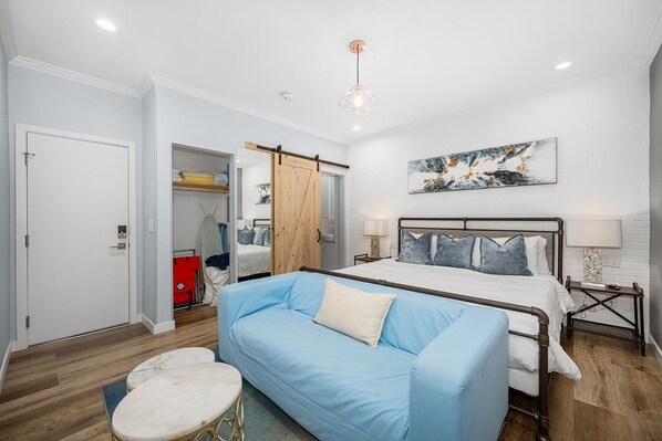 A bedroom with a bed, a blue sofa, a wooden wardrobe, and a painting on the wall.