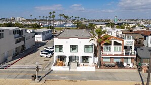A coastal hotel with a white facade, a balcony with outdoor seating, and a view of the marina. - West Oceanfront Oasis 1-2-3 (Newport Beach)