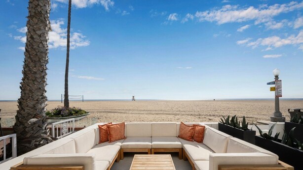 A beachside seating area with a sofa and a wooden table, overlooking the beach. - West Oceanfront Oasis 1-2-3 (Newport Beach)
