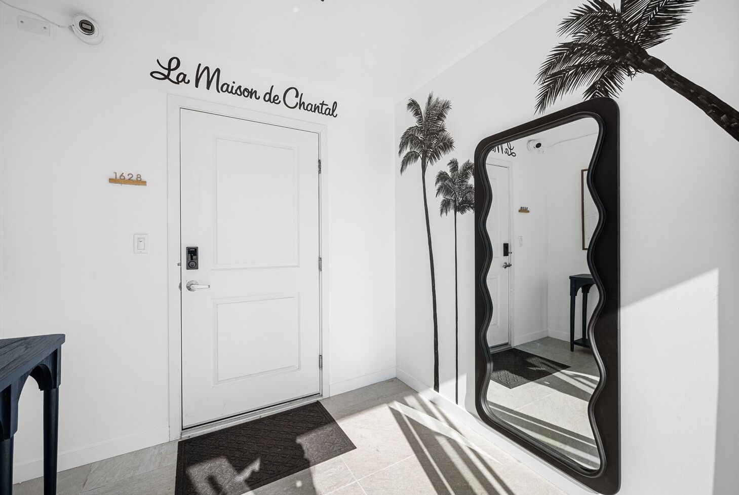 A hallway with a white door, a black-framed mirror, and a palm tree decoration.
