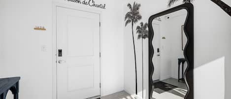 A hallway with a white door, a black-framed mirror, and a palm tree decoration.