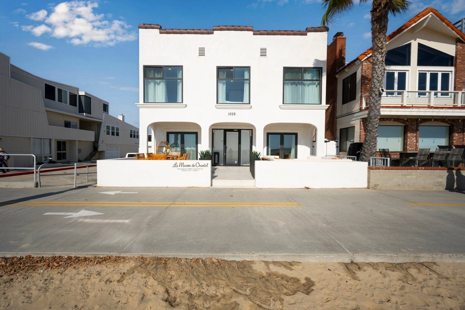 Un immeuble de deux étages avec une façade blanche, de grandes fenêtres et un balcon doté de sièges pour l’extérieur.