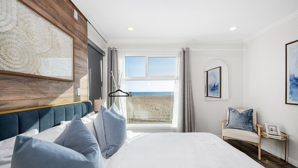 A bedroom with a large bed, a view of the beach, a chair, and a side table. - 1628 West Oceanfront Oasis - 4-6-7 (Newport Beach)