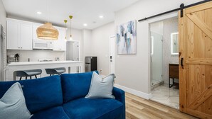 A modern living room with a blue sofa, a kitchen with white cabinets, and a wooden sliding door. - 1628 West Oceanfront Oasis - 4-6-7 (Newport Beach)