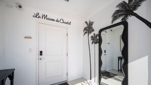 A hotel entrance with a white door, a black-framed mirror, and palm tree wall art.
