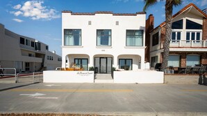 Un immeuble de deux étages avec une façade blanche, de grandes fenêtres et un balcon doté de sièges pour l’extérieur.