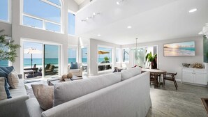 A spacious living area with large windows, a high ceiling, and a view of the ocean. - Oceanfront Family Home with Firepit on the Sand (Capistrano Beach)