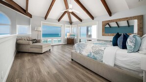 A bedroom with a large bed, a sofa, a TV, and a view of the ocean. - Oceanfront Family Home with Firepit on the Sand (Capistrano Beach)