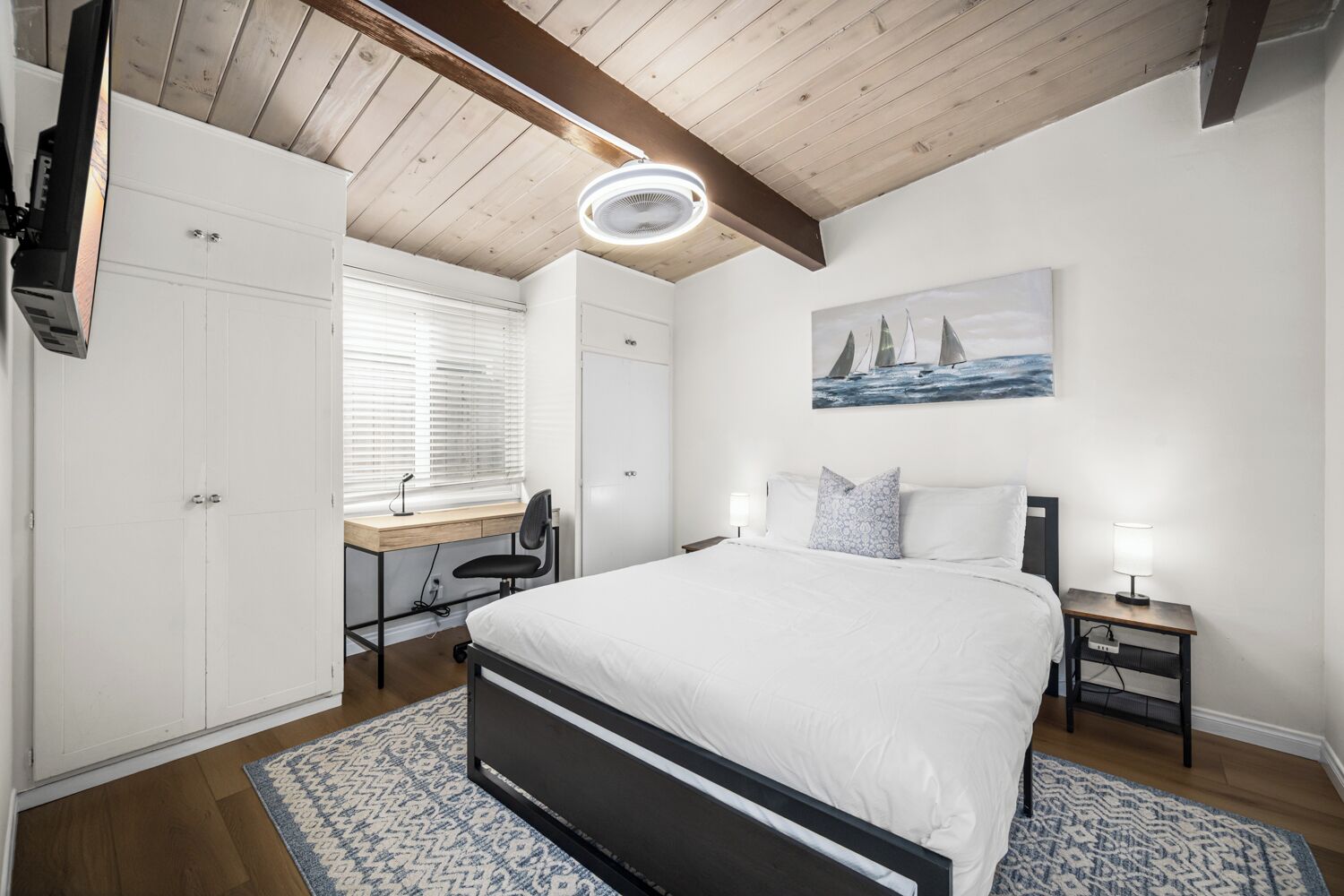 A bedroom with a bed, a desk, a chair, a computer, and a painting on the wall.