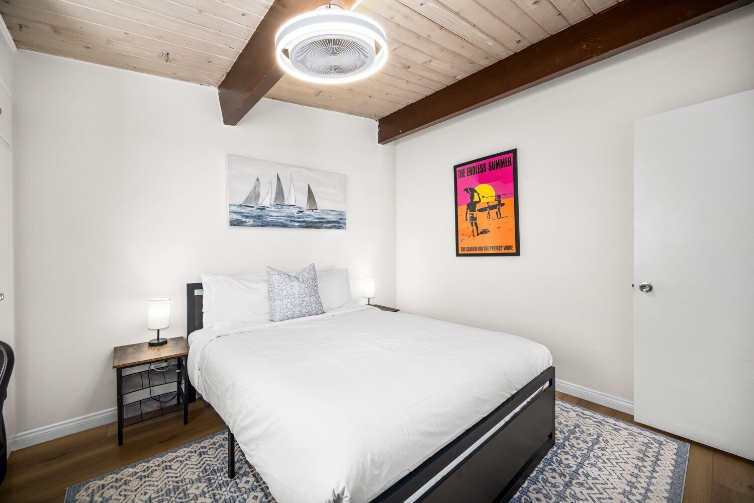 A bedroom with a bed, a nightstand, a lamp, a poster, and a door.